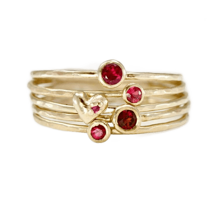 Stack of hammered gold rings with ruby-red stones and a gold heart